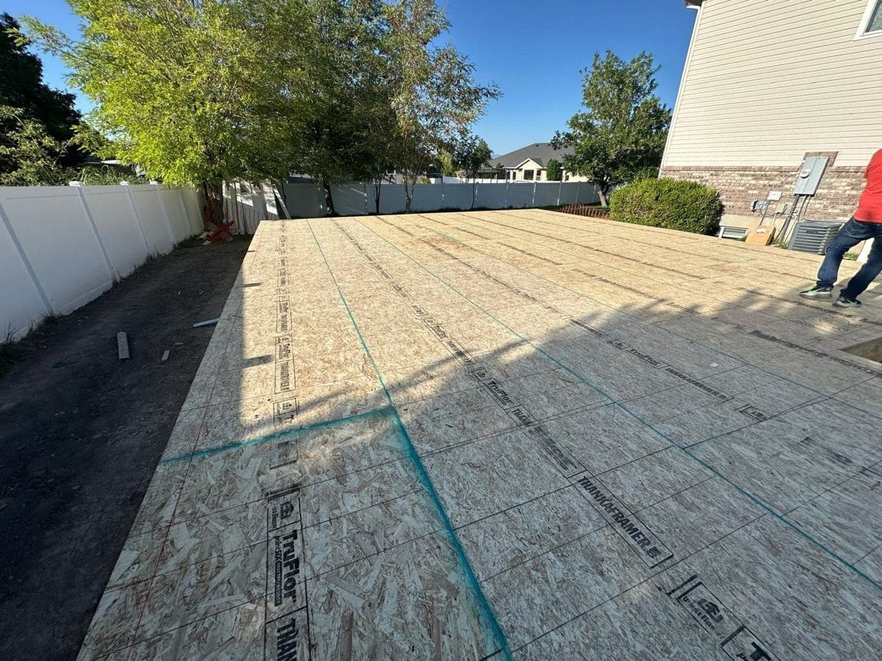 Subfloor decking installed over a new concrete foundation next to a vinyl fence
