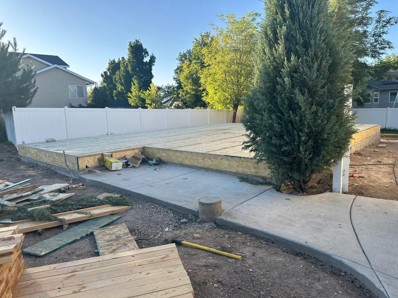 Lumber and pressure-treated boards staged beside the subfloor and new concrete walkway