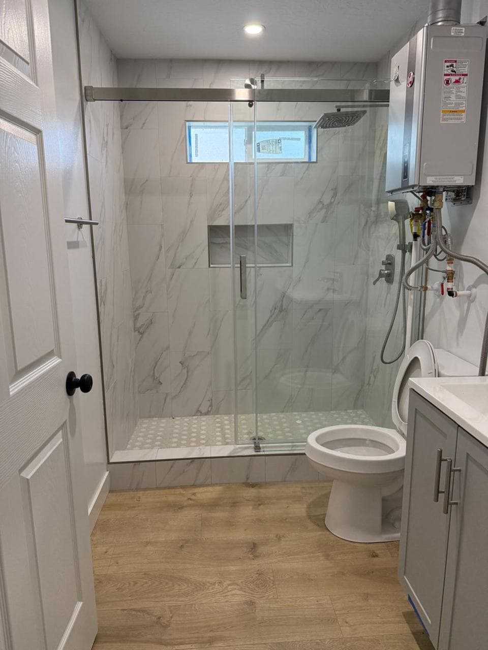 Finished walk-in tiled shower with glass door, niche and tankless water heater
